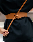 Esquel Belt in caramel full-grain leather, visible front tie over black outfit.
