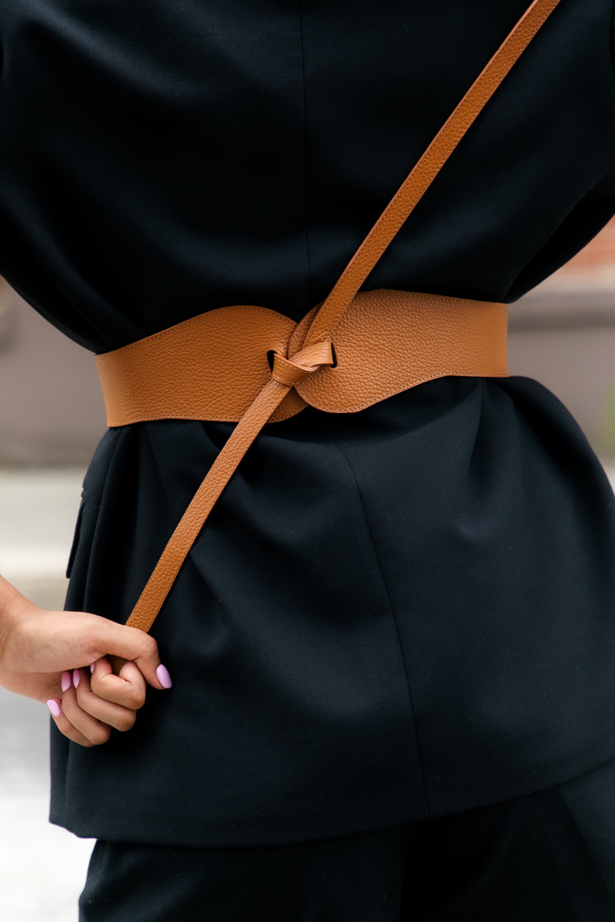 Esquel Belt in caramel full-grain leather, visible front tie over black outfit.